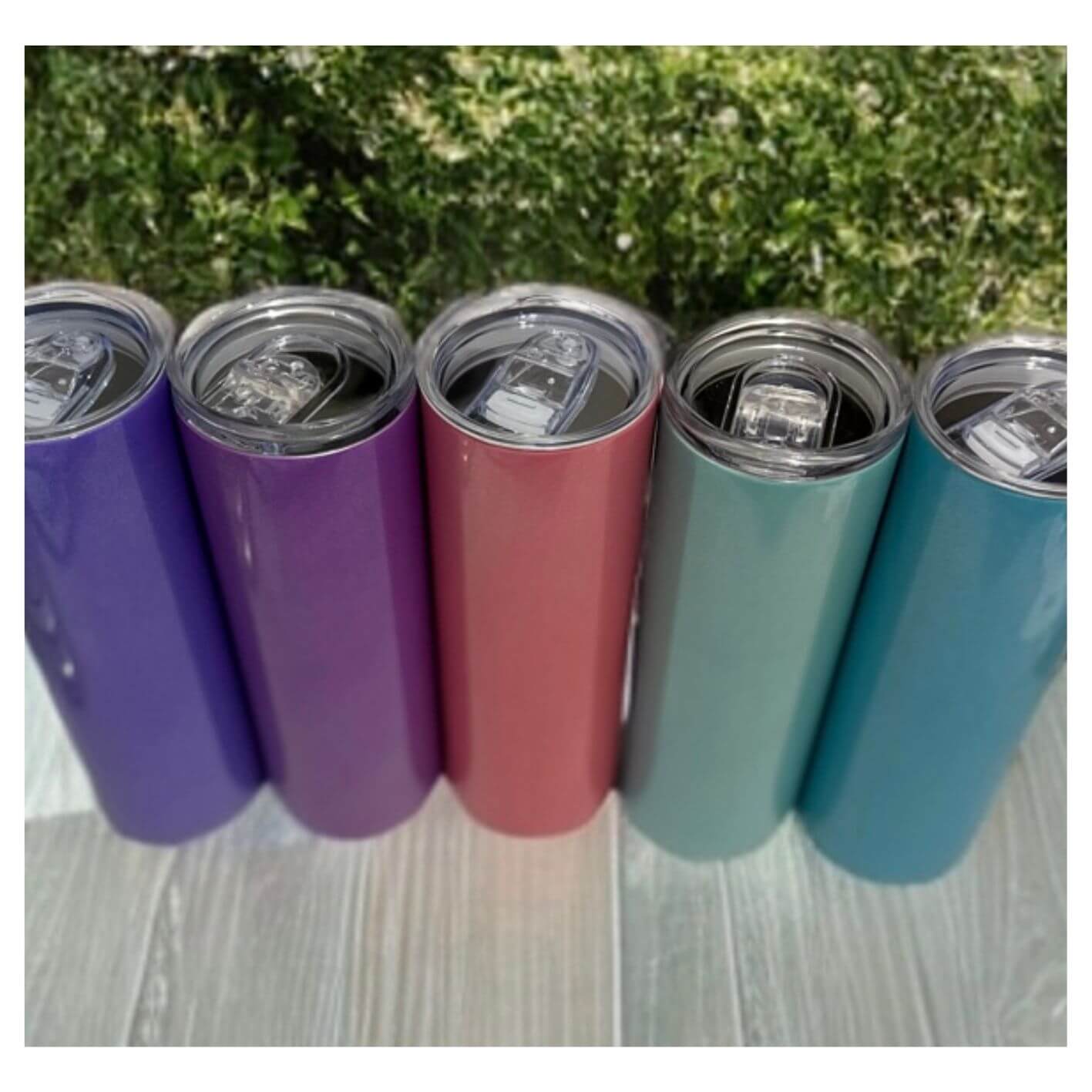 Five colorful tumblers on a wooden surface with a green outdoor background