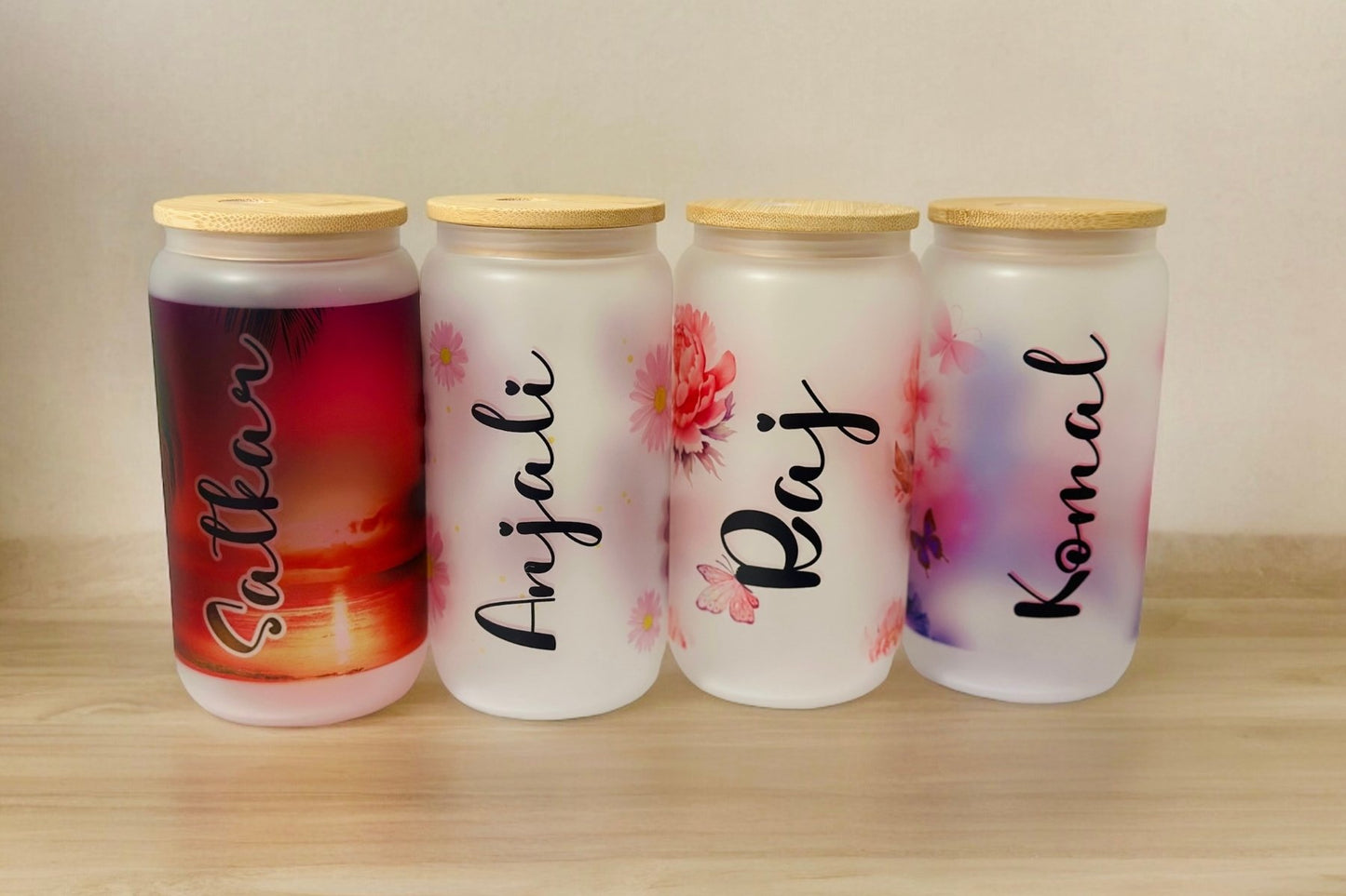 Four glass tumblers with wooden lids, each featuring a different name and floral design.