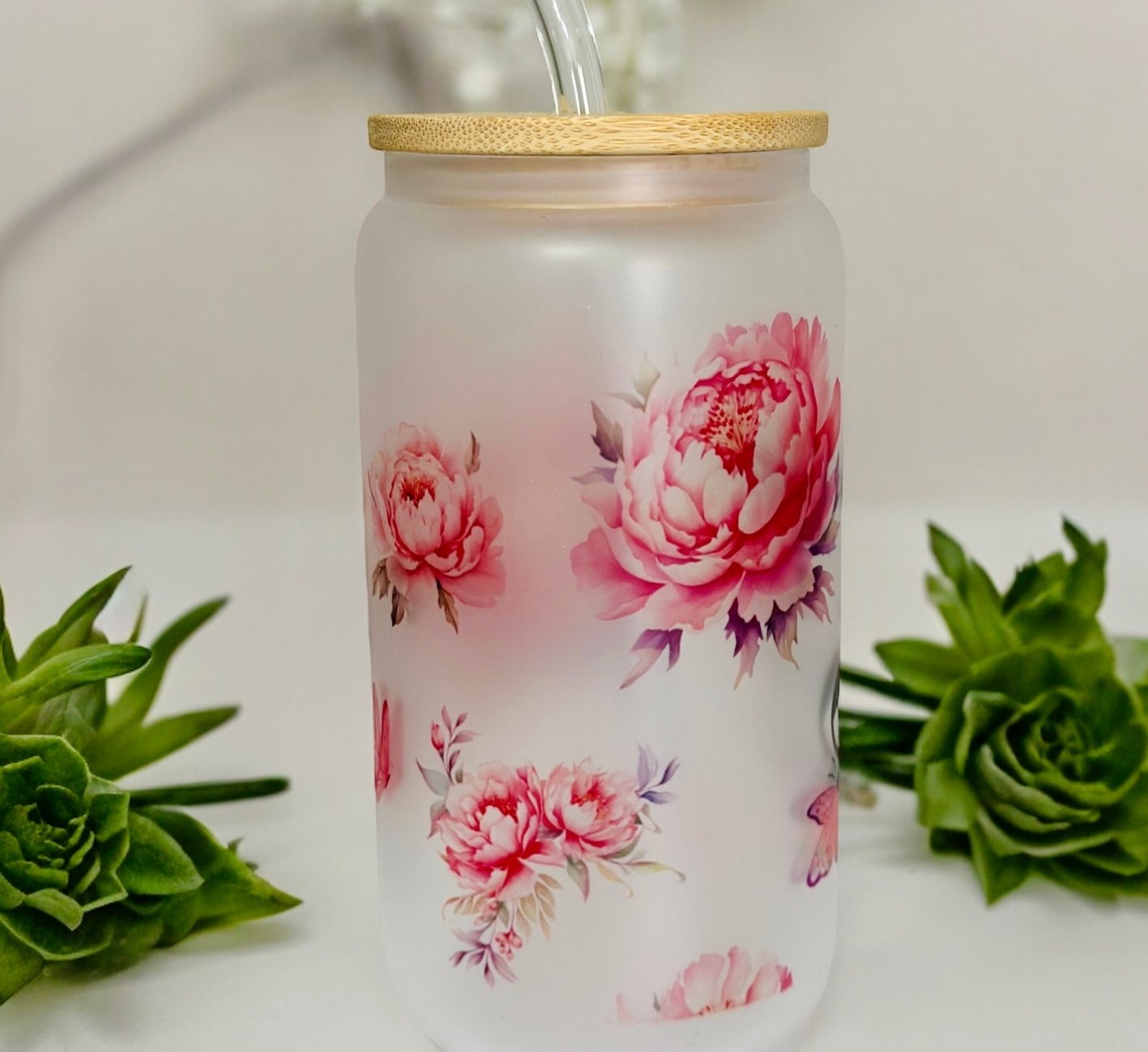 Tumbler with floral design and bamboo lid on a white background with green plants.
