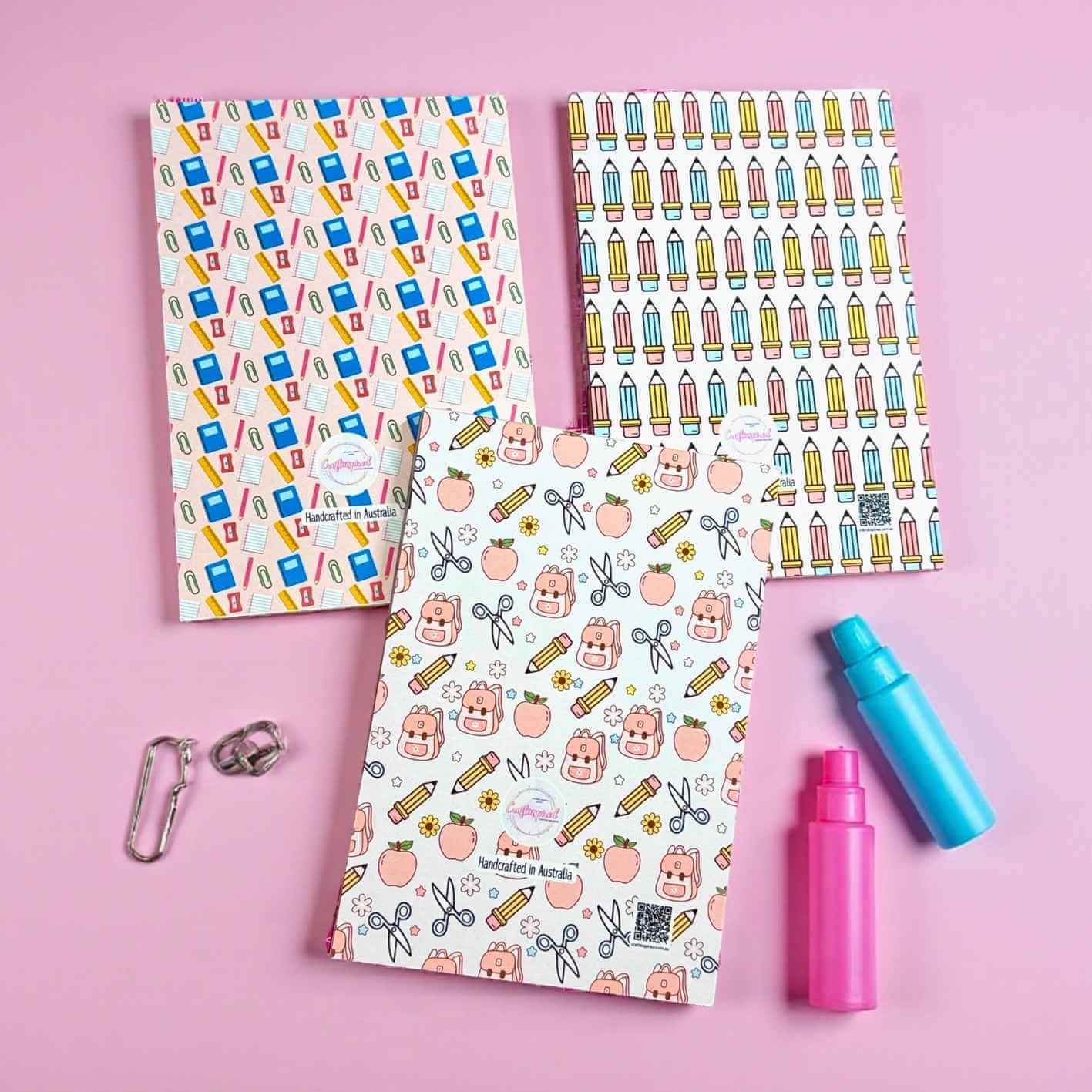 Three cute backing of note pads with different designs on a pink background, surrounded by small stationery items