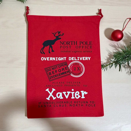 Red gift bag with Christmas-themed text and graphics on a light wooden surface.