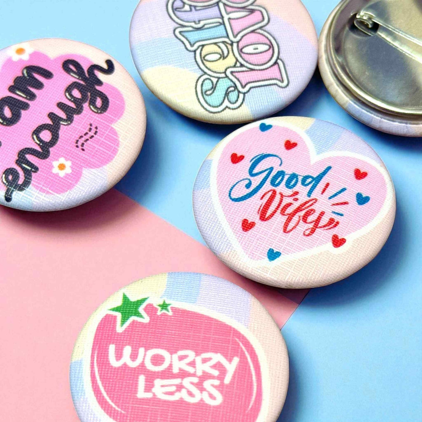 Close-up of positive vibes button pin badges showing detailed designs including 'I am enough', 'Self Love', 'Good Vibes', and 'Worry Less' with metal pin backs - custom motivational badges
