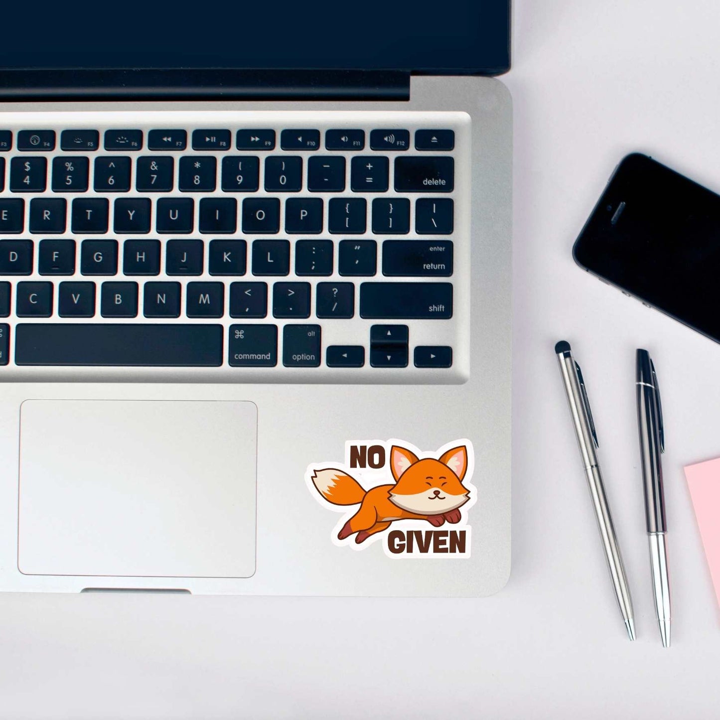 Laptop with a 'No Fox Given' sticker on a desk with pens and a phone.