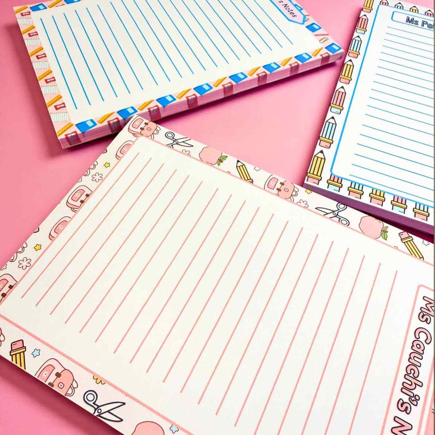 Set of lined notepads with colorful stationery-themed border on a pink background