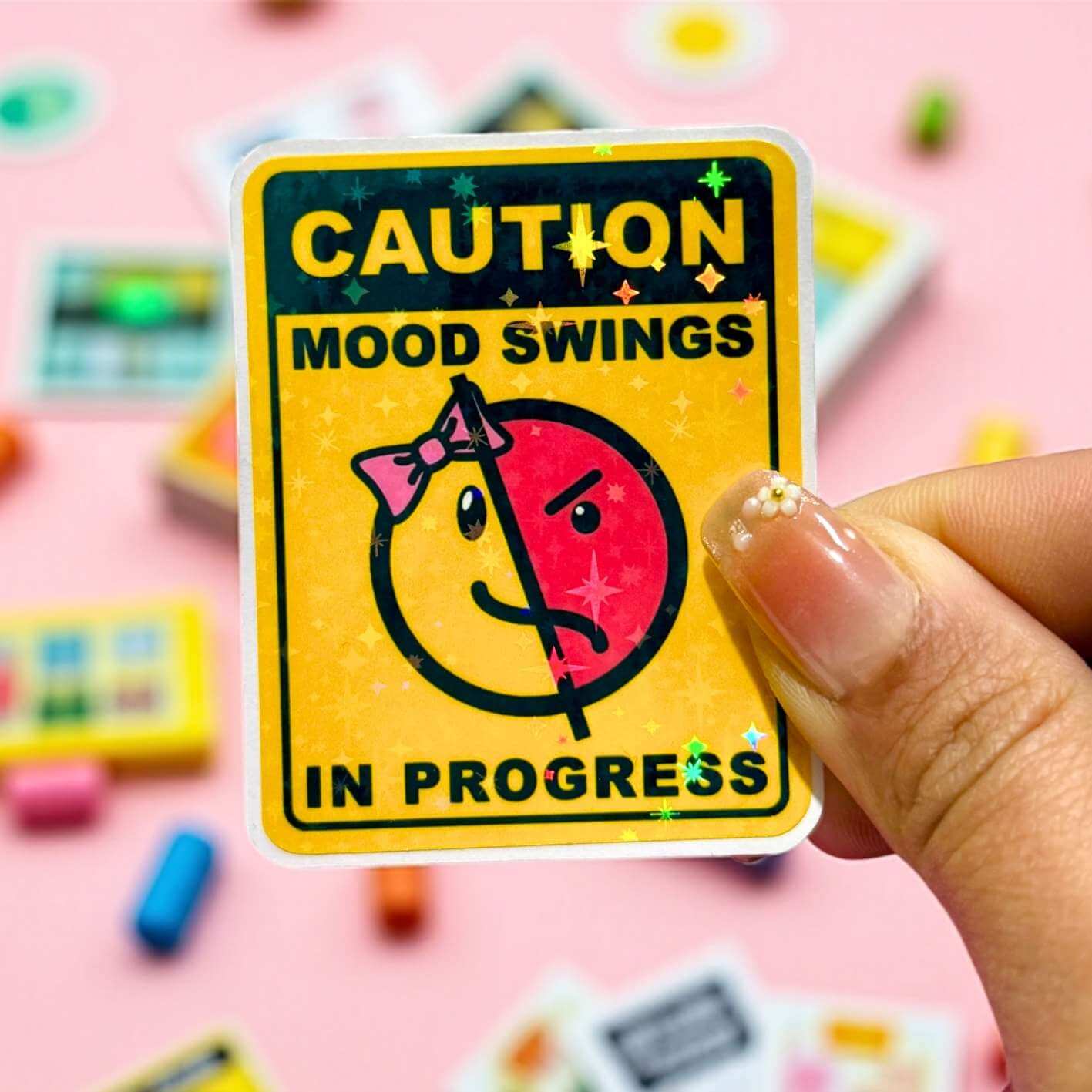 Sticker with 'Caution: Mood Swings in Progress' text held by a hand on a colorful background