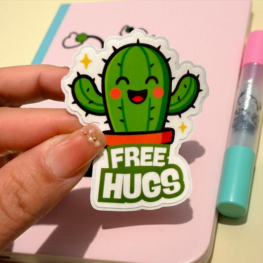 Sticker of a cactus with 'FREE HUGS' text held by a hand on a pink background.