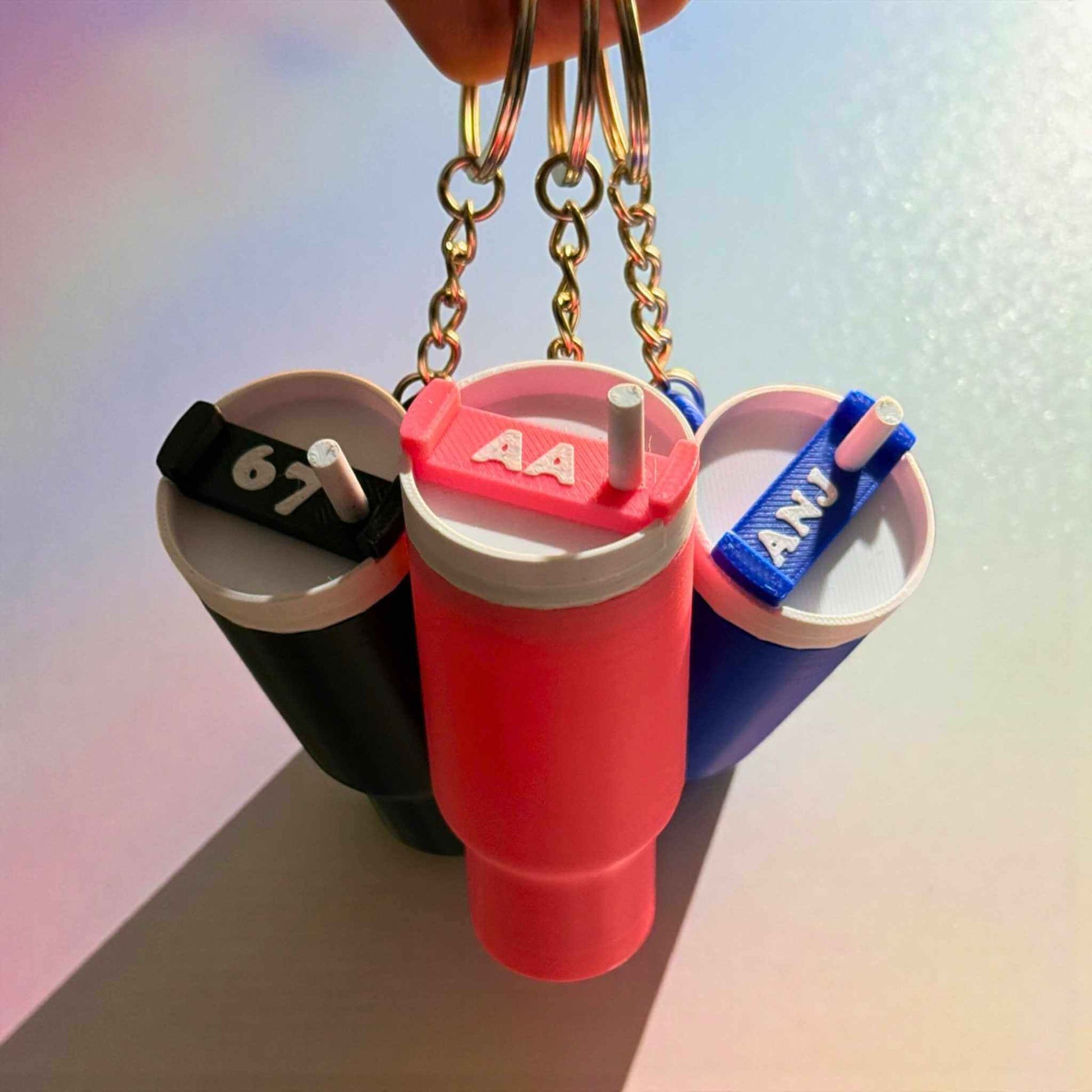 Three colourful keychains shaped like drink containers with 'AA' personalisation on a gradient background.
