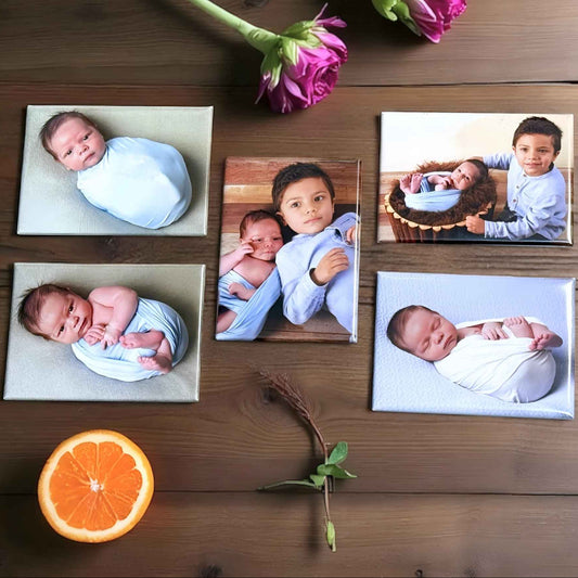 Collection of baby photos on a wooden surface with flowers and an orange.