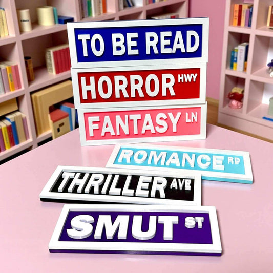 Stack of genre-themed road signs on a pink surface with bookshelves in the background