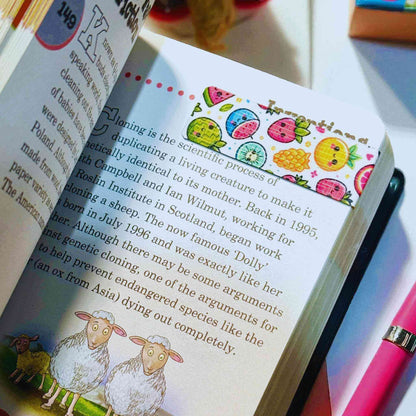 Handmade magnetic bookmark featuring adorable fruit characters including watermelon, pineapple, and orange in practical use on open book - reading gifts delivered across Australia