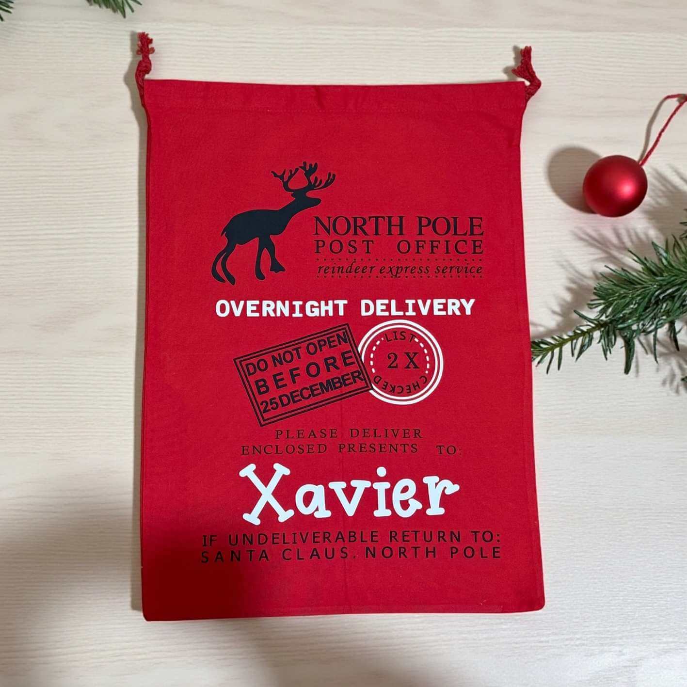 Red gift bag with Christmas-themed text and graphics on a light wooden surface.