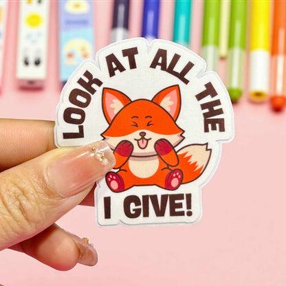 Sticker with a fox design and text held by a hand against a colourful background
It says look at all the FOX PHOTO I give