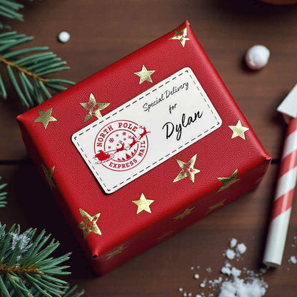 Red gift box with gold stars and a personalised label on a wooden surface with Christmas decorations.