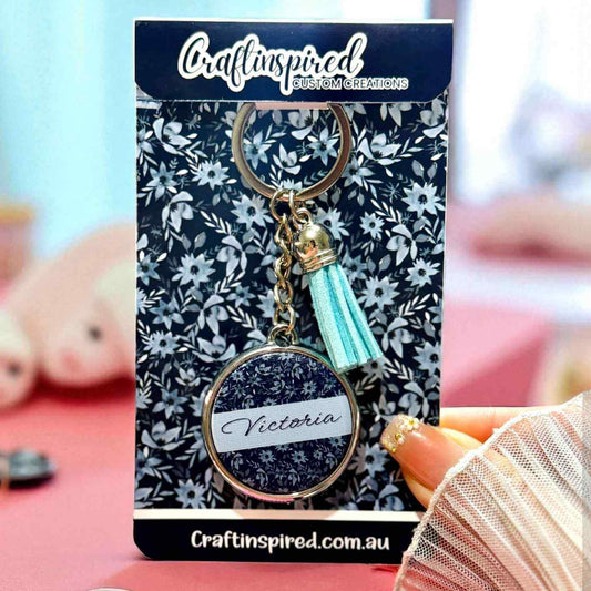 Custom keychain with 'Victoria' on a floral card, packaging brand 'Craftinspired' visible.