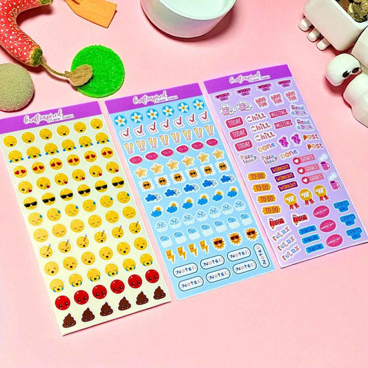 Three sheets of emoji and colourful aesthetic kawaii planner stickers on a pink surface with small decorative items.
