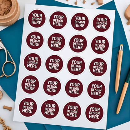 Sheet of round stickers with 'Your Design Here' text on a blue surface with stationery items.  