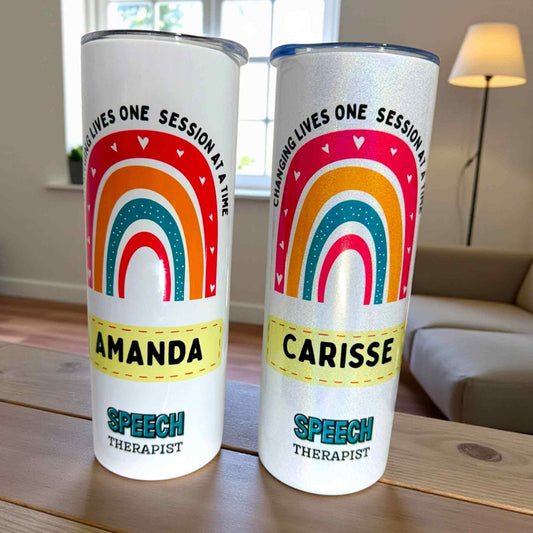 Two tumbler cups with rainbow designs and personalized names on a wooden surface.