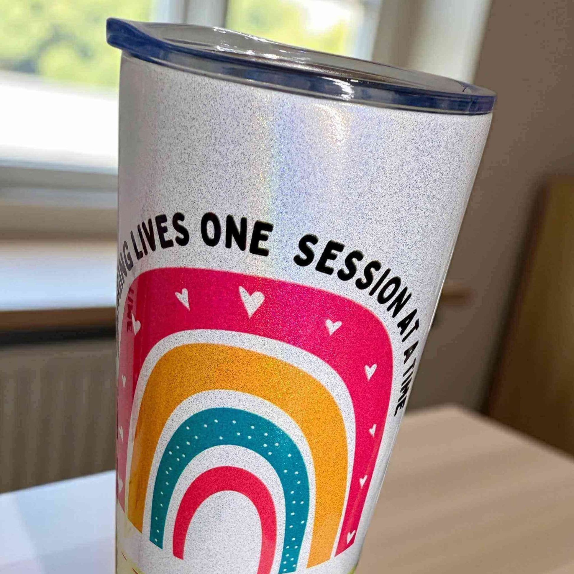 Tumbler with colourful design and text on a table glittery finish